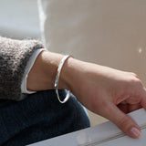 Person wearing a hammered silver bracelet on a neutral background