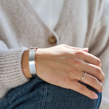 Hand wearing a silver bracelet and ring, with a neutral background