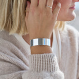 Person wearing a wide silver cuff bracelet on a neutral background