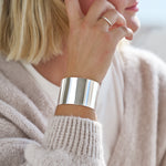 Person wearing a large silver cuff bracelet on a blurred background