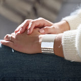 Close-up of a hammered silver cuff bracelet on one arm and a blurred background