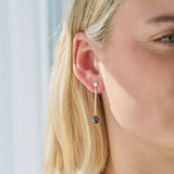 Close-up of a woman wearing silver dark pearl drop earrings against a neutral background