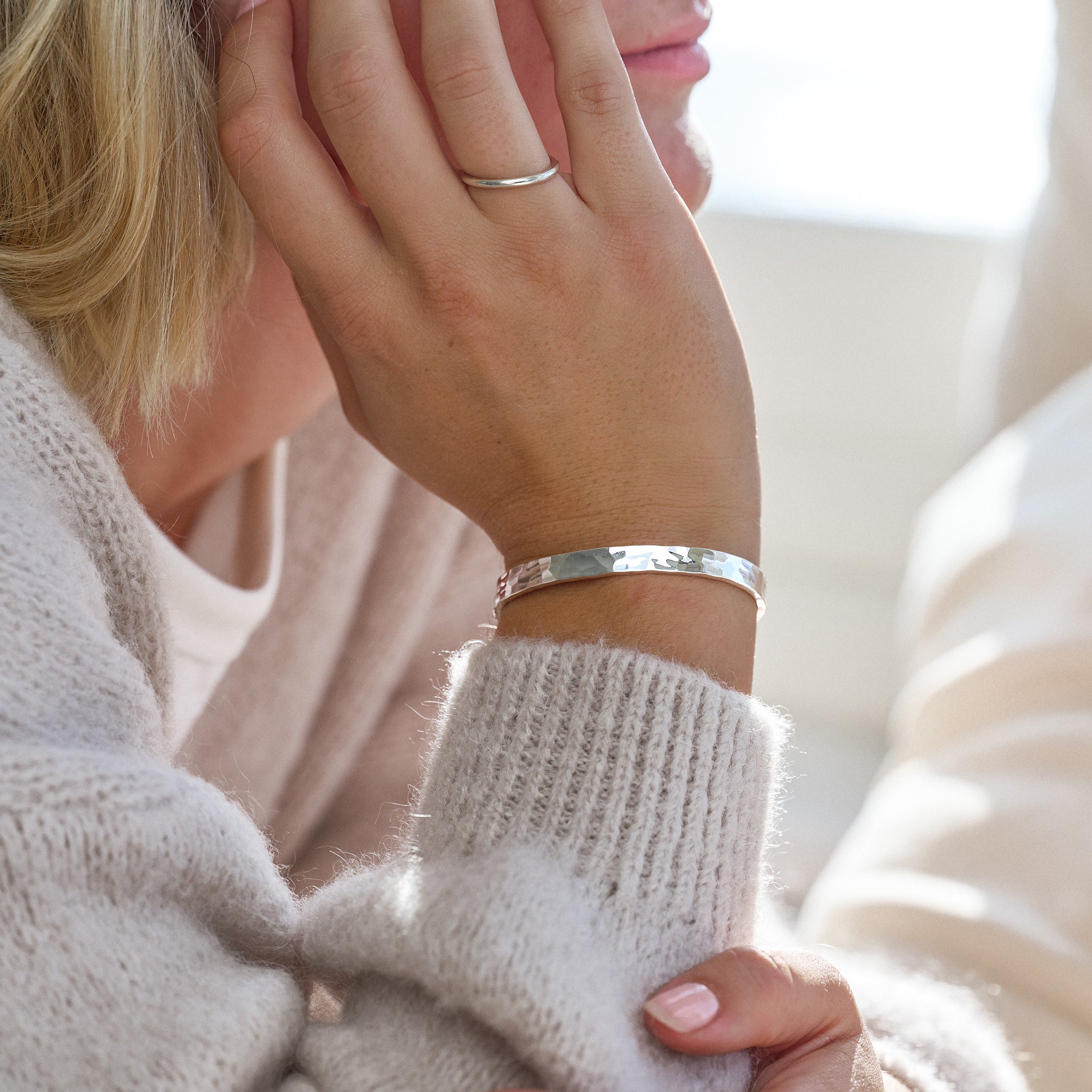 Close-up of a person wearing a hammered silver bracelet and ring, with a blurred background.