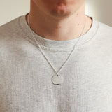 Person wearing a silver necklace with a round pendant on a plain background