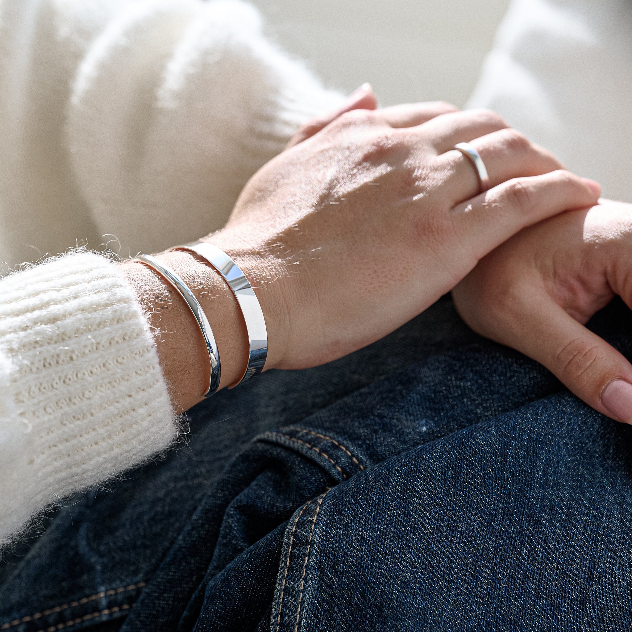Close-up of hands wearing silver bracelets and a ring, with a blurred background.