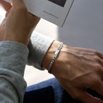 Person wearing a silver chain bracelet on a neutral background holding a book