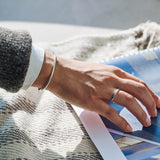 Person wearing a silver bracelet with a silver ring on their finger