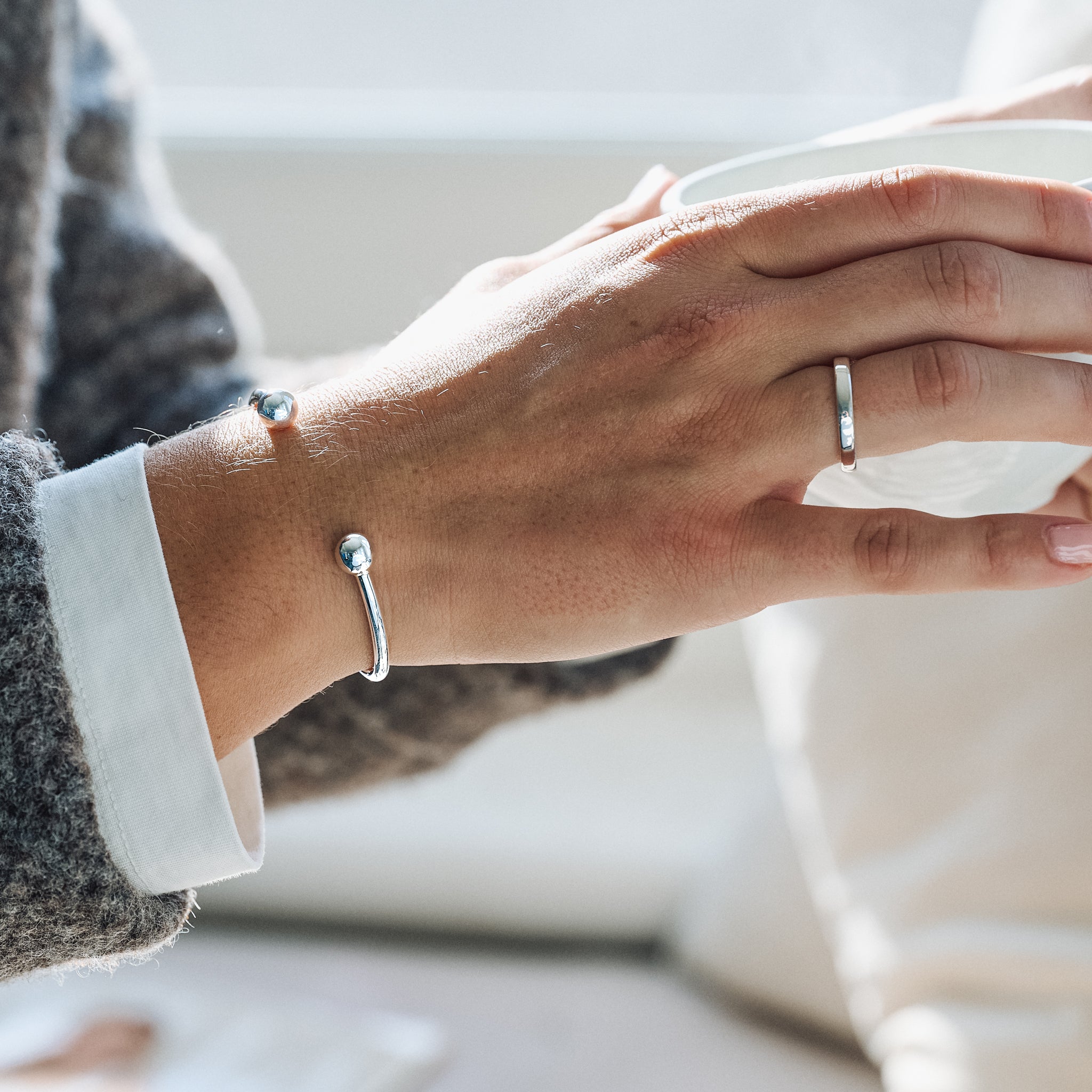 Close-up of hands wearing silver rings and bracelets on a blurred background