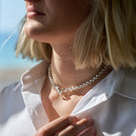 Close-up of a person wearing a silver box chain necklace with a t-bar clasp on a blurred background
