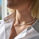 Close-up of a person wearing a silver box chain necklace with a blurred background