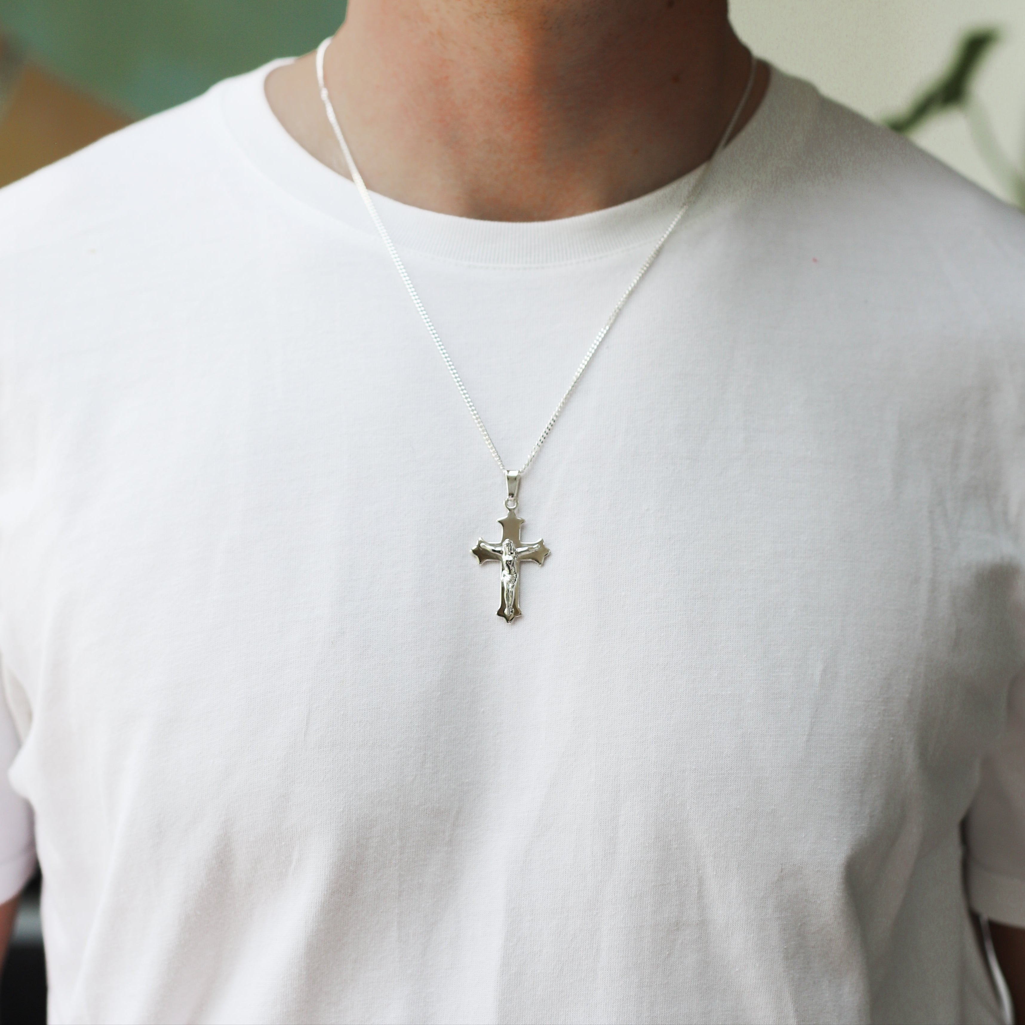 Person wearing a white t-shirt with a cross pendant necklace.