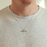 Person wearing a silver necklace with a pendant on a plain background