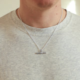 Person wearing a silver necklace with a pendant on a plain background
