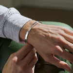 Close-up of a person wearing a silver hammered bracelet resting arm on green sofa