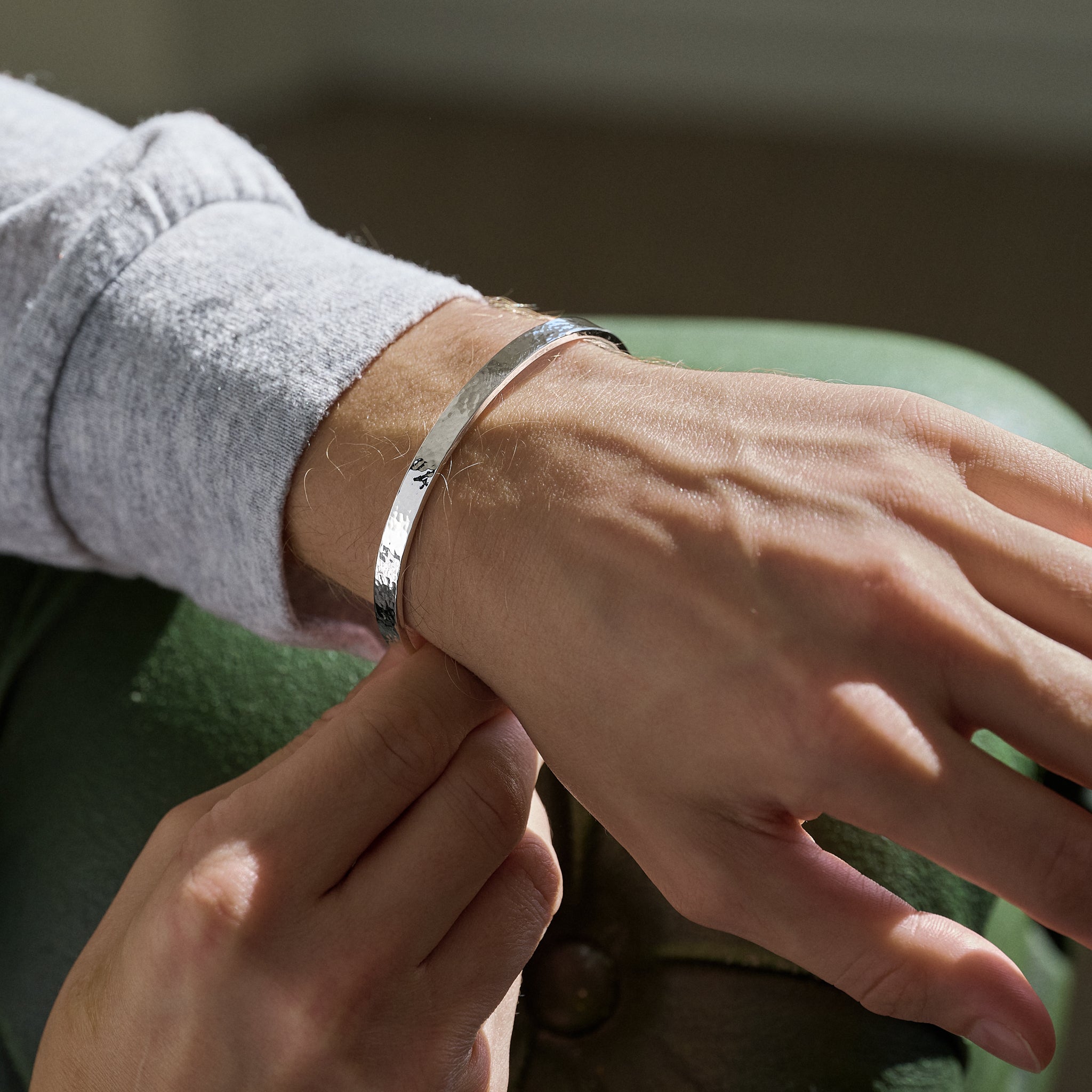Close-up of a person wearing a silver hammered bracelet resting arm on green sofa