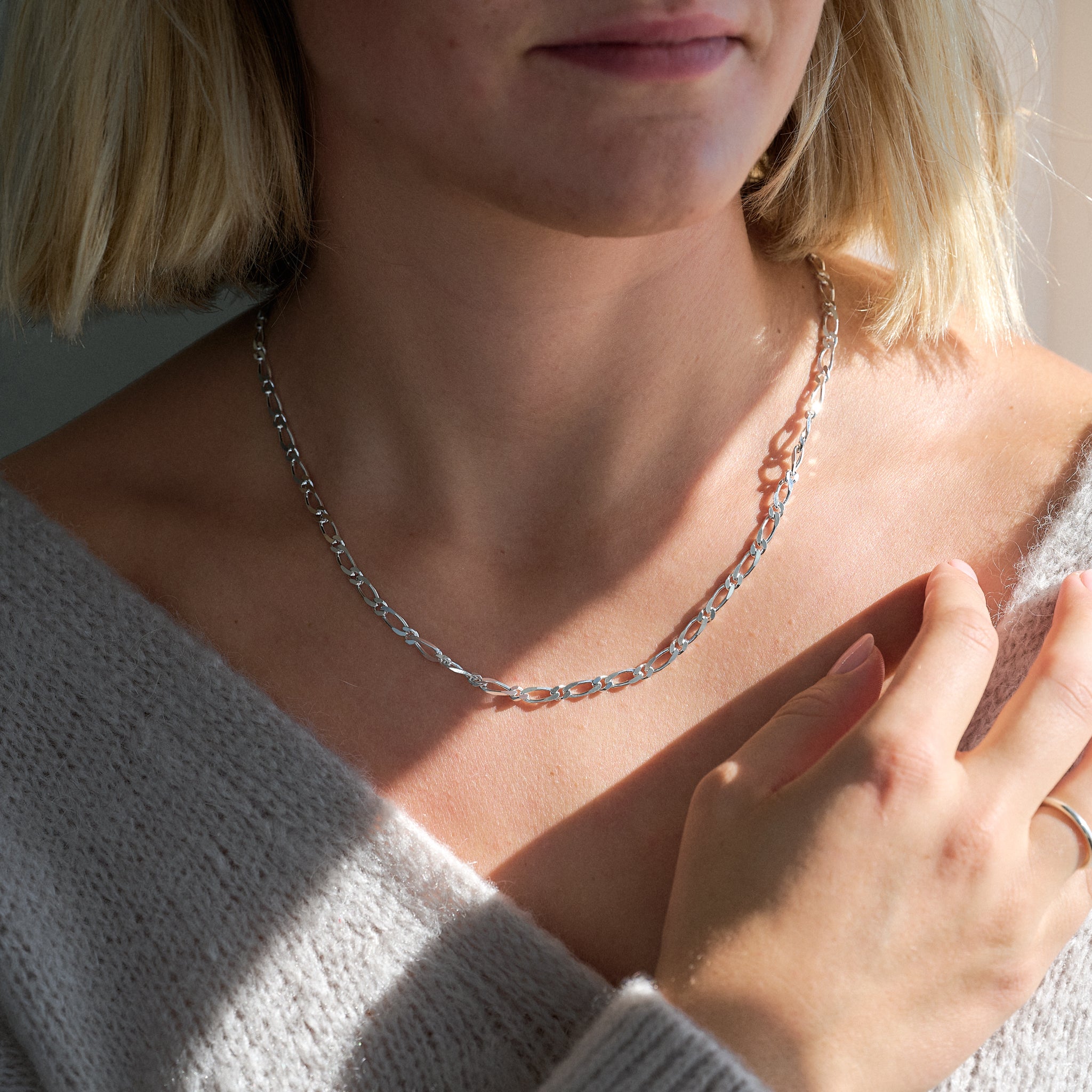 Close-up of a person wearing a silver chain necklace and light grey cardigan.