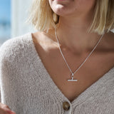 Woman wearing a silver necklace with a t-bar pendant, blurred background