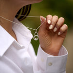Person wearing a white shirt holding a silver necklace with interlocking rings.