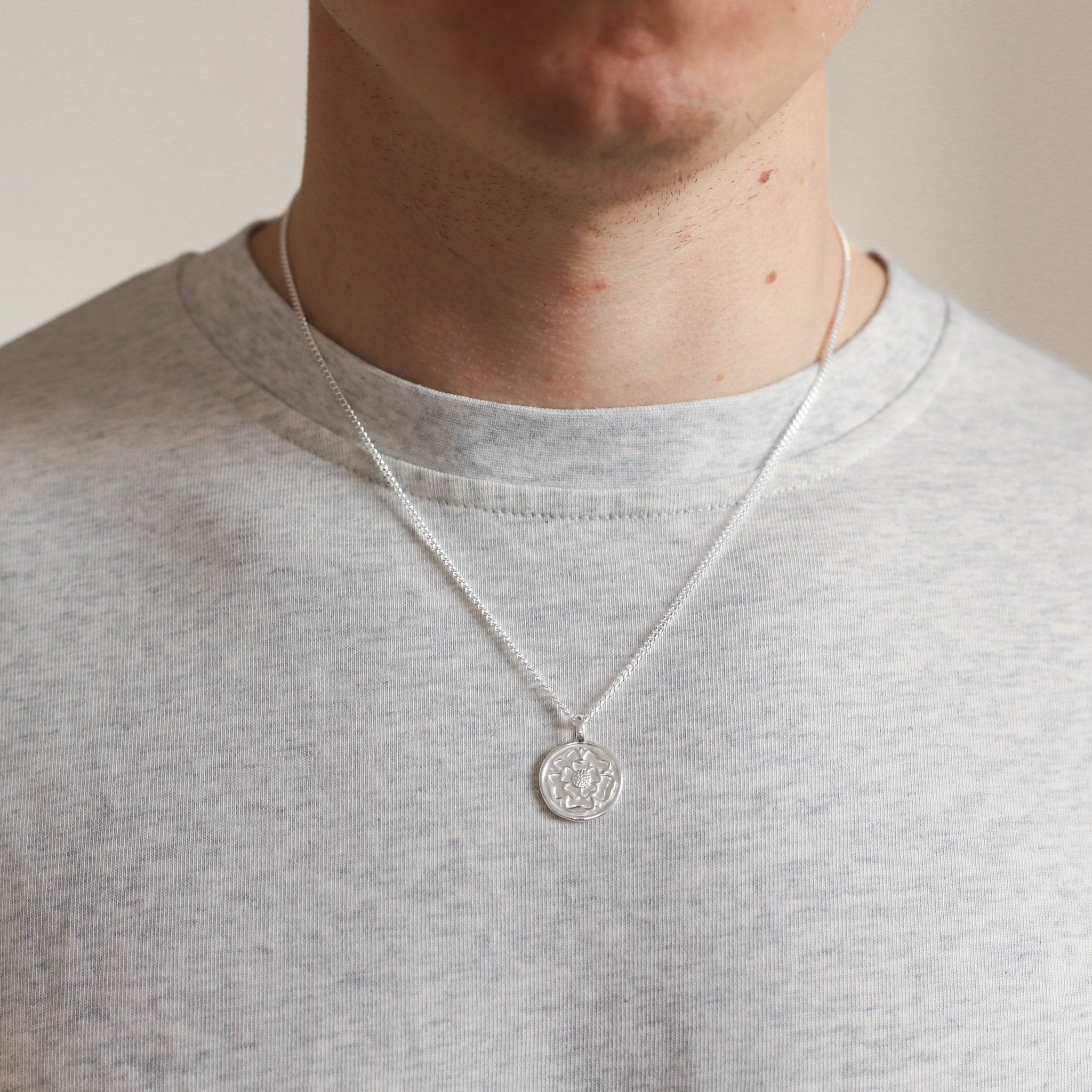 Person wearing a silver necklace with a round pendant on a plain background