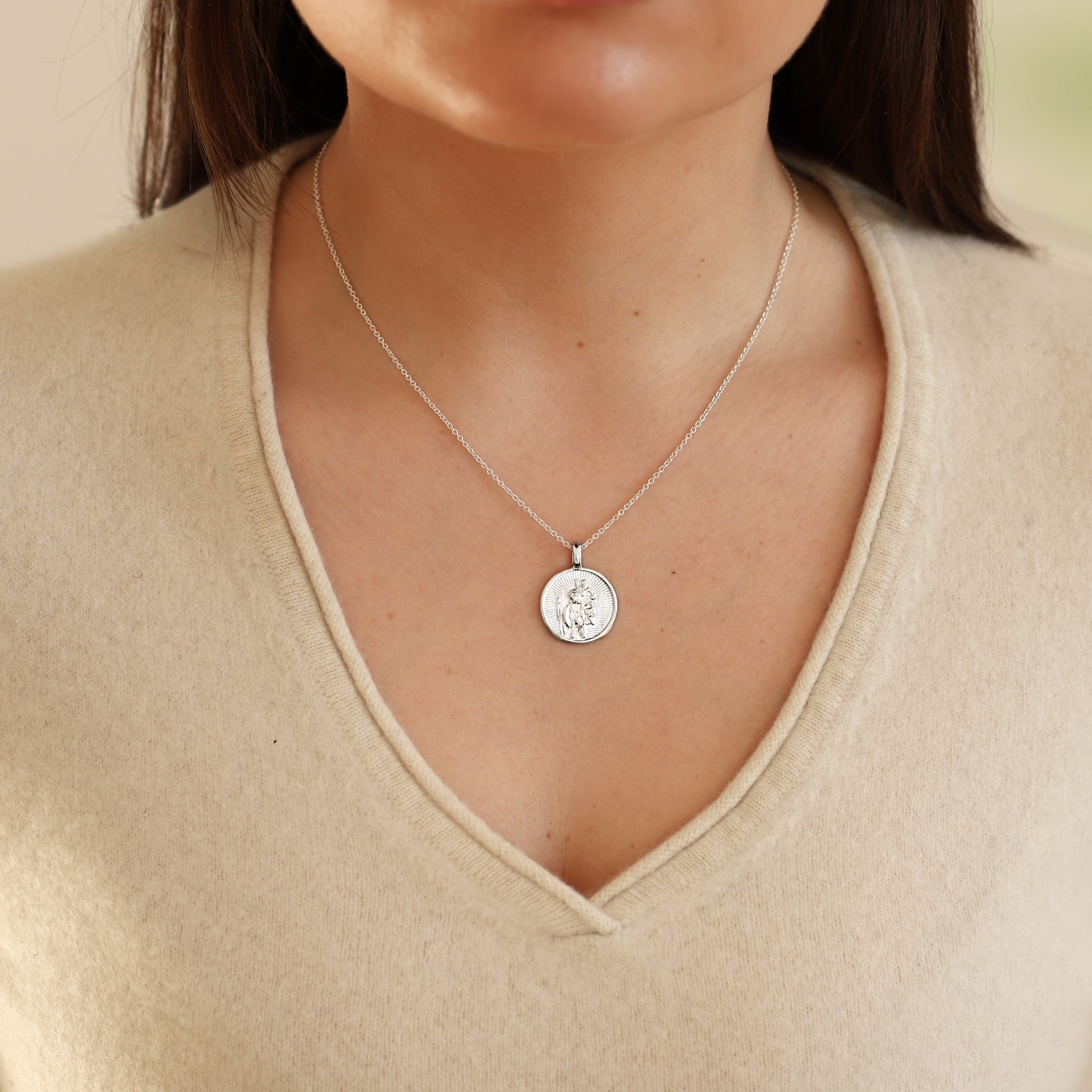 Necklace with a round pendant worn by a person in a beige sweater.
