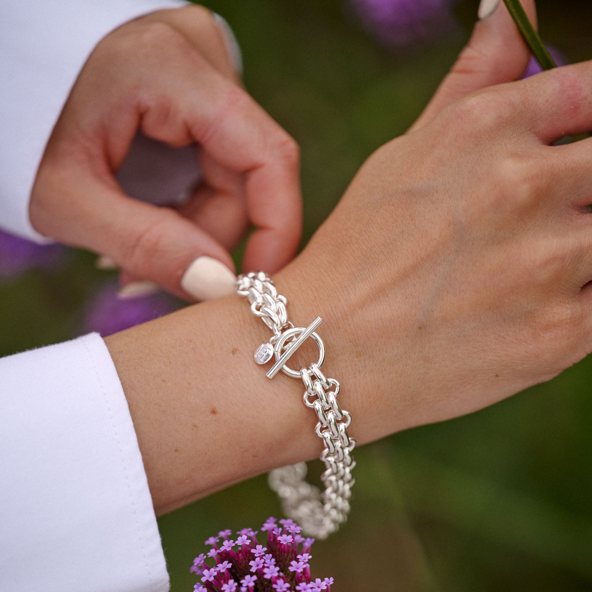 Close-up of a person wearing a silver bracelet with a floral background