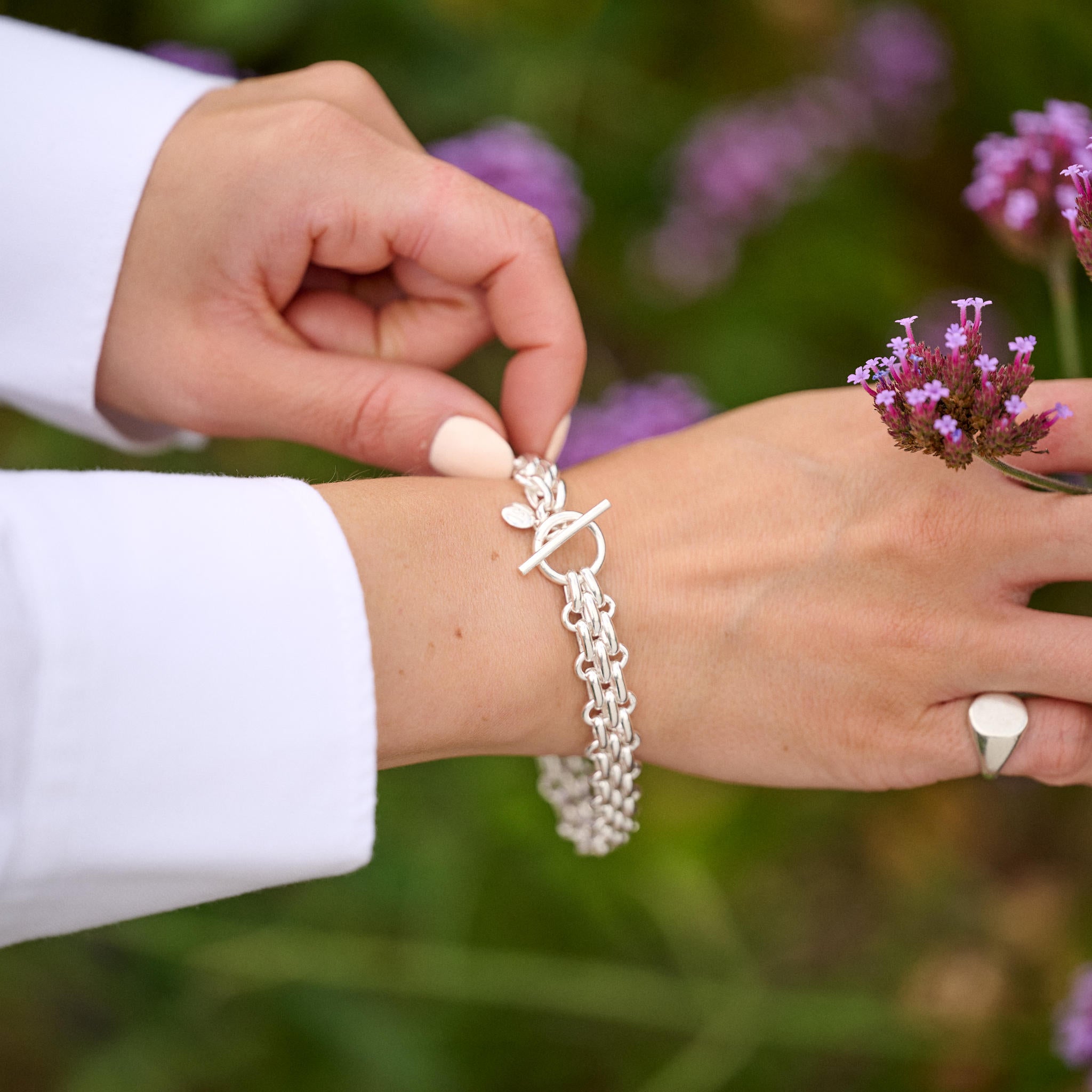 Person wearing a silver bracelet with a blurred floral background