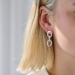 Close-up of a person wearing a silver triple linked earrings with a blurred background