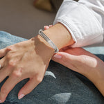 Person wearing a silver wired bracelet in a white shirt and blue jeans