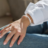 Close-up of a hand wearing a silver wired bracelet on a blurred background