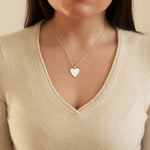 Heart-shaped pendant necklace worn by a person in a beige sweater.