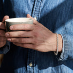 Person holding a mug in a denim shirt with silver chain bracelet on wrist