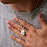 Person wearing a silver necklace with a round pendant, held by a hand.