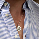 Close-up of a necklace with a pendant on a person wearing a blue and white striped shirt.