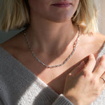Close-up of a person wearing a silver chain necklace and light grey cardigan.