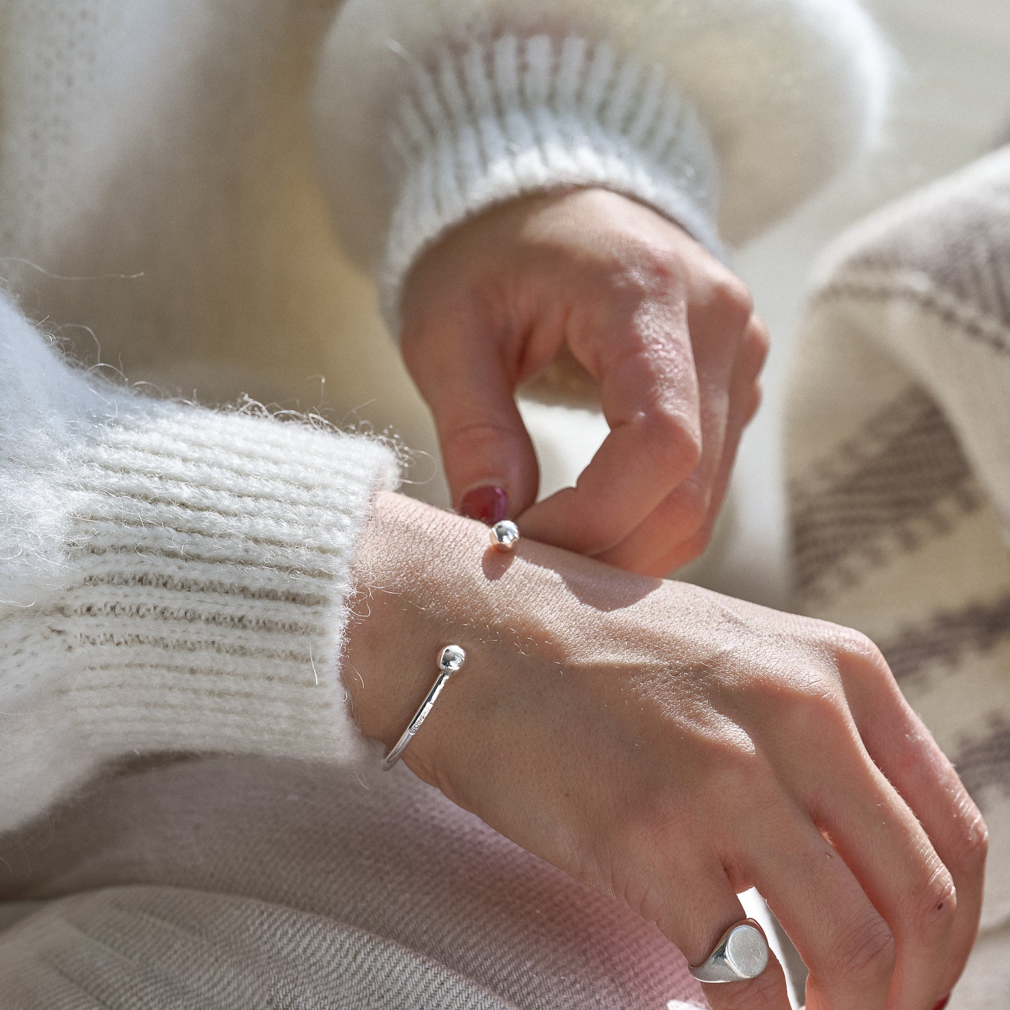 Close-up of a person wearing a silver ball cuff bracelet and rings in a coloured sweater
