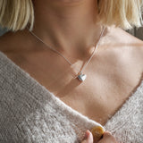 Close-up of a person wearing a silver heart-shaped locket necklace.