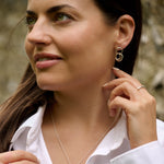 Woman wearing silver hoop earrings and a necklace, with a blurred natural background