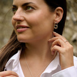 Woman wearing silver hoop earrings and a necklace, with a blurred natural background