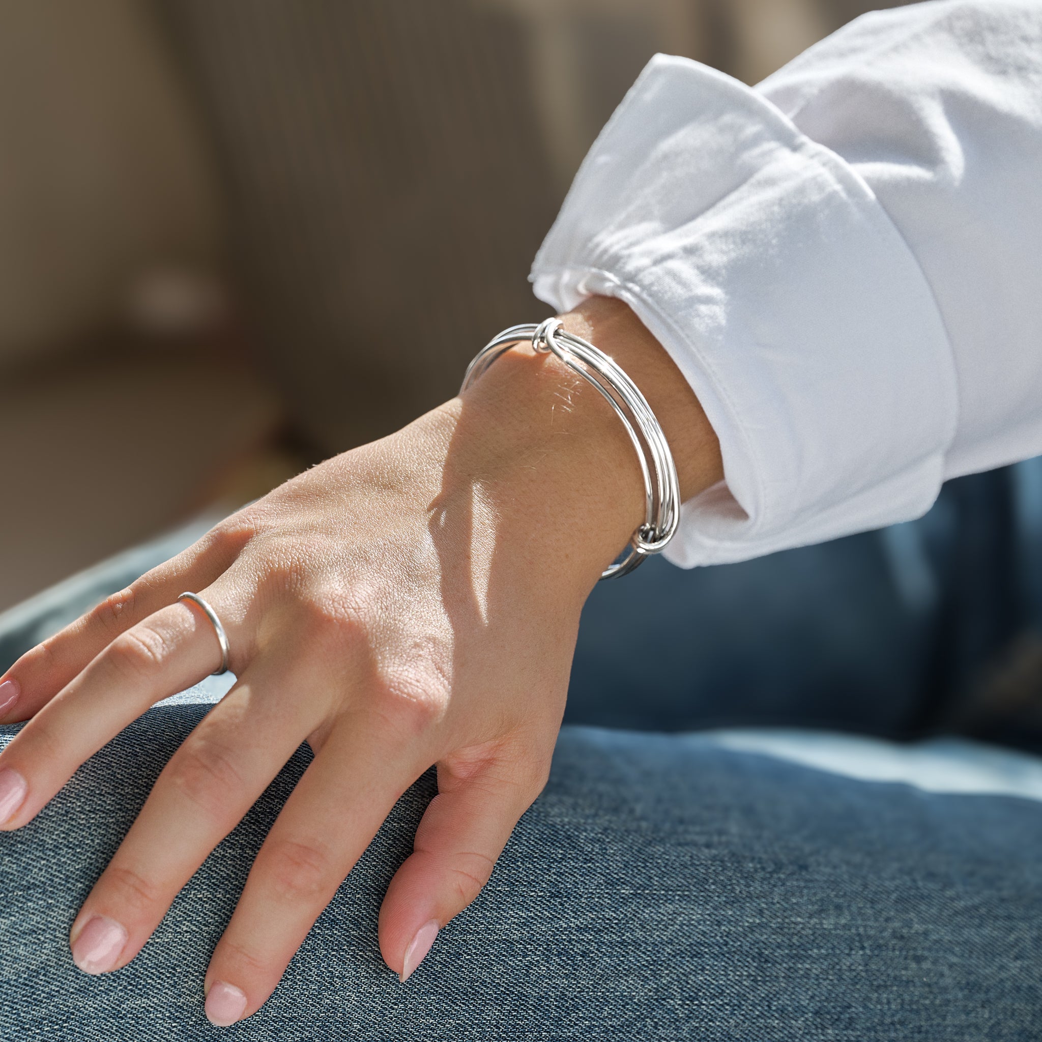 Close-up of a hand wearing a silver wired bracelet on a blurred background