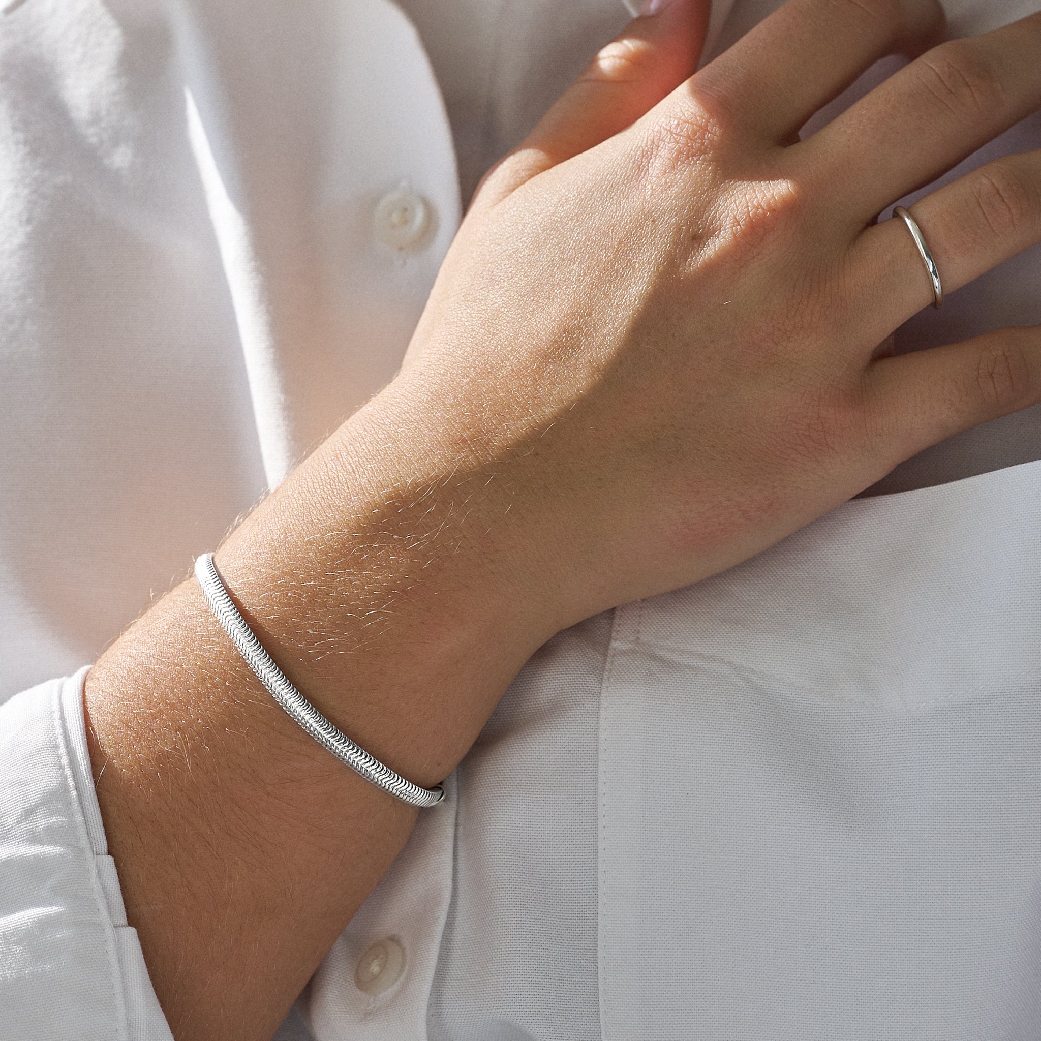 Close-up of a hand wearing a silver snake bracelet and ring on a white shirt background