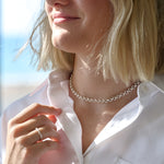 Close-up of a person wearing a silver chain necklace with a blurred background